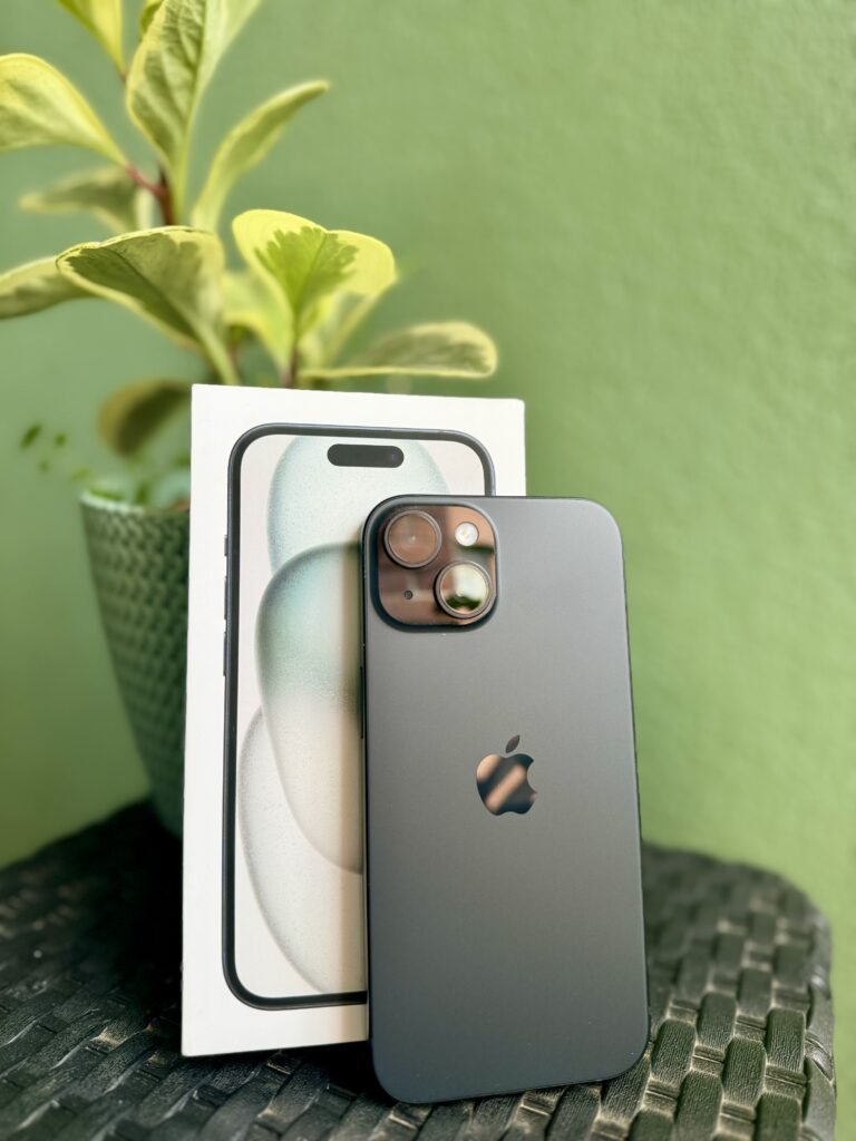 iPhone 15 Black displayed in front of iPhone 15 case with a small plant in the background.